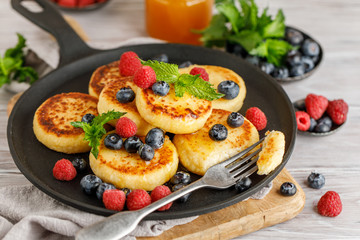 Cottage cheese pancakes with raspberry and blueberry in pan on rustic background, breakfast or lunch