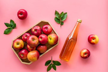 Apple cider vinegar in glass bottle and wooden tray with red apples