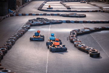 Three guys overtaking each other on an indoor karting track - obrazy, fototapety, plakaty