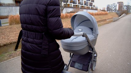 Unrecognizable mother walks while pushing stroller. Autumn clothing. High quality photo