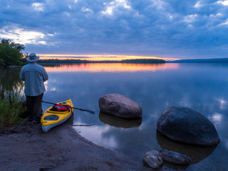 Man standing by kayak at sunrise on lake

