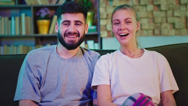 Very attractive couple at home in the sofa watching a tv comedy they smiling large and have a fun time together