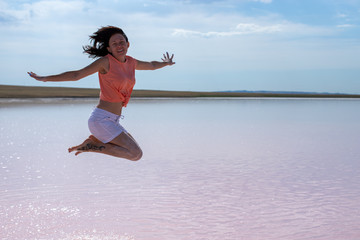 Brunette in a jump wearing a pink top and white shorts with her face, arms and legs covered with salt against the background of the pink Lake Kobeituz in north Kazakhstan's Akmola Region.