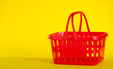 Empty red plastic shopping basket on yellow background