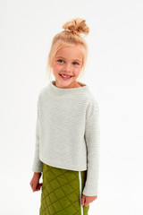 Cheerful blonde girl with a bun on her head smiles with a toothless smile on a white background in a sweater with a strip and a green skirt