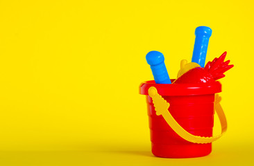 Baby set red sandbox bucket shovel rake toy on yellow background