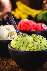 vegan avocado, banana and raspberry ice creams, without preservatives or added milk. With tropical fruits in the background, in handmade clay bowl.