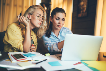 Focused young couple of female colleagues using laptop in flat