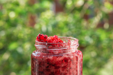 Jar of fresh red currant jam on blurred summer background