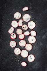 Sliced radishes sprinkled with salt and spices on a dark wet background