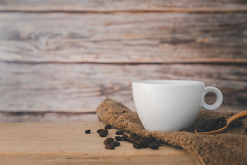 A white hot coffee cup and coffee beans with a spoon and a saucer are placed on a wooden plate and on a wooden background.front view.