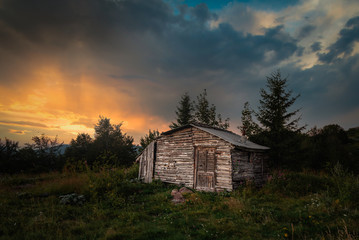 Old abandoned wooden house in the mountains, and beautiful sunset scene in background.