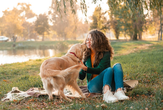 Smiling woman hugging her pet golden retriever dog near face. Golden retriever dog playing with a curly woman walking outdoors sunny day. love and care for the pet.