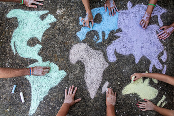 A group of people drawing with colored chalks on the floor with his hands in the street a map of...