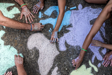 A group of people drawing with colored chalks on the floor with his hands in the street a map of...
