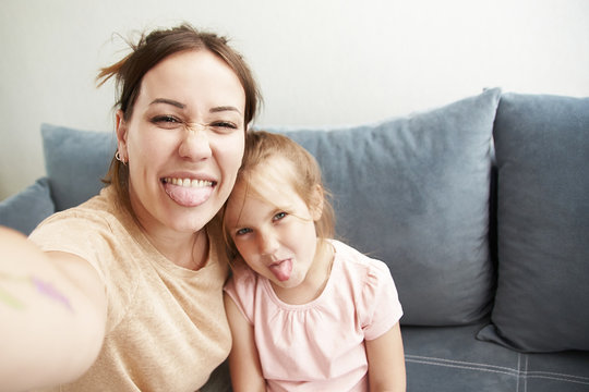 Cute mom and daughter take selfies and fool around in the phone camera. A girl portrays a monster, and mom shows tongue