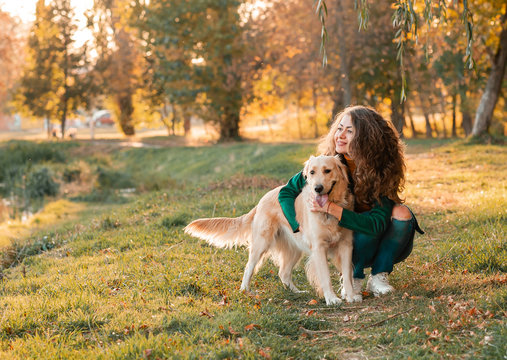 Golden retriever dog with a curly woman walking outdoors on sunny day. Training the dog in the park. love and care for the pet.
