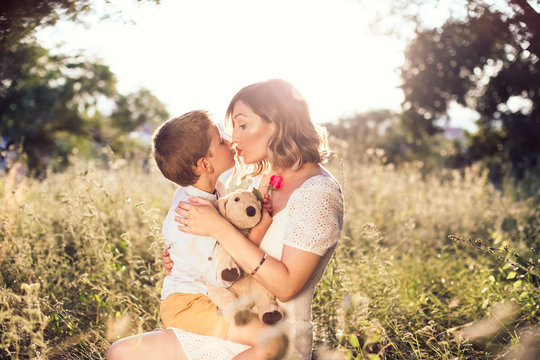 Young mom kissing her son on the lips. Boy holding a rose for his mom.