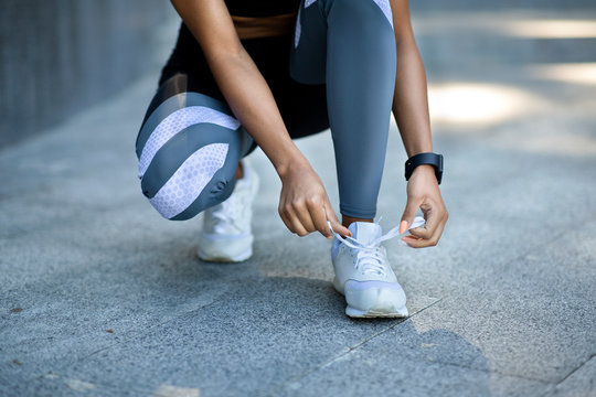 Closeup of black girl in sportswear tying shoelaces before jogging