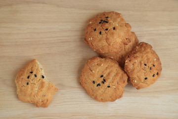Tasty sesame cookies on wooden plate, one bitten piece.