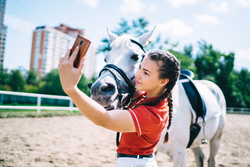 Horsewoman taking selfie with stallion on smartphone