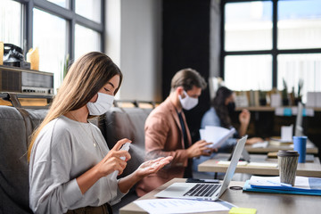 Portrait of young businesspeople with face masks working indoors in office, disinfecting hands.