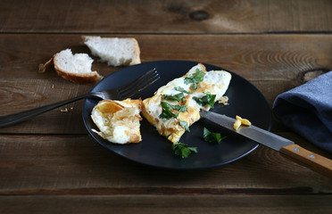 Omelet on a plate with herbs. A fork, a knife, and a blue towel lie nearby.