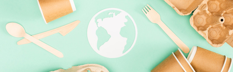 Panoramic shot of disposable tableware and paper earth sign on green background, ecology concept