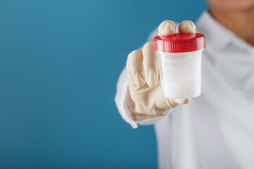 A doctor's gloved hand holding a bottle of a container with a sperm sample for medical analysis.