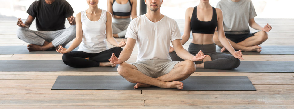 Group Of People Doing Yoga Exercises Together, Practicing On Mats In Studio