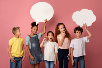 Cute multinational schoolchildren with empty speech bubbles over pink background, space for design