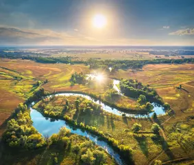 Foto op Canvas Aerial view of beautiful curving river at sunrise in summer. View from air. Turns of river, green meadows, grass and trees, blue sky, sun at dawn.  Colorful aerial landscape of river coast. Top view © den-belitsky
