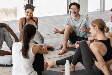 Group of multiracial young people communicating before yoga class in studio
