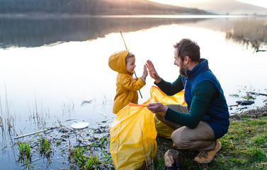 Father with small daughter collecting rubbish outdoors in nature, plogging concept.