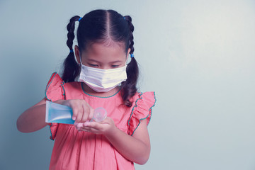 Asian kid girl wearing a medical mask using alcohol gel cleaning hands for protection coronavirus Covid-19.