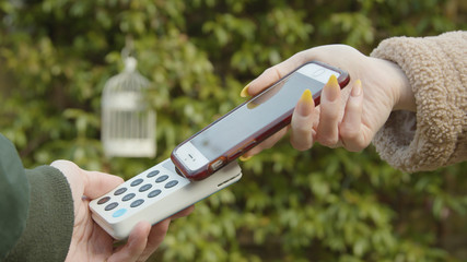 Contactless payment with a smart phone outside an independent cafe female hand