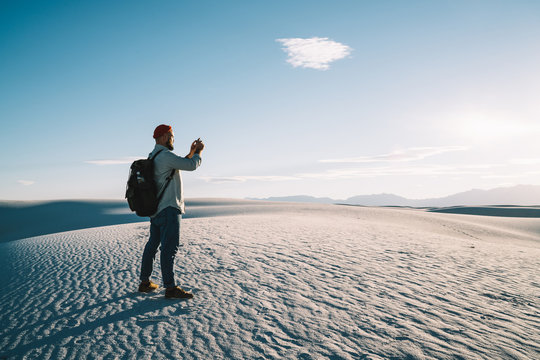 Caucasian male influencer taking image on smartphone camera exploring nature environment of white desert during vacation trip, hipster guy wanderlust taking photo for travel blog using mobile phone