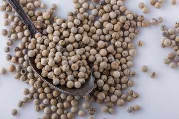 white peppercorns in spoon on white background