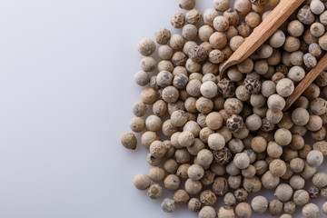 white peppercorns in wooden scoop on white background