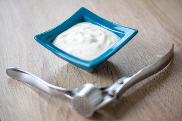 Bowl with garlic sauce and a garlic press on a wooden table