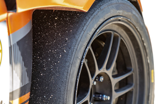 A sports car wheel with a worn slick tire with adhered asphalt close-up and orange parts of the car in the sun. Horizontal orientation. High quality photo