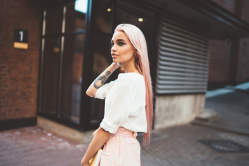 Thoughtful female youngster with colored pink hair standing at city urbanity and thinking, contemplative Caucasian hipster girl 20 years old pondering on information during day walk in soft focus