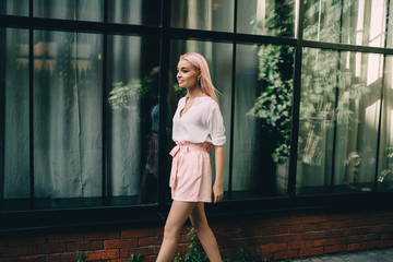 Side view of casual dressed hipster girl 20s walking at urban setting enjoying leisure time for visiting touristic town, attractive Caucasian female with colored pink hair going at city street