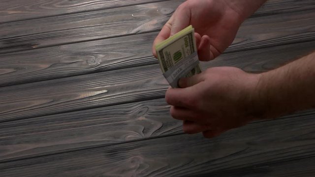 Bundle of dollars falling on wooden table. Male hand taking dollars bundle. Bribery concept.