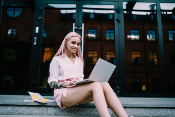 Portrait of cheerful female student sitting at city urbanity with modern laptop computer and education textbook for doing distance e learning, youthful freelance journalist smiling at camera
