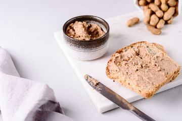 Homemade peanut paste or butter in a bowl and bread and peanuts on white marble tray. Healthy nutrition. Selective focus
