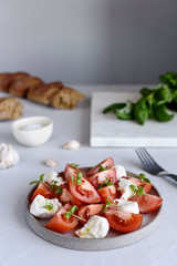 Italian Сaprese salad with sliced tomatoes, mozzarella cheese, basil, olive oil in a plate on grey concrete table. Selective focus