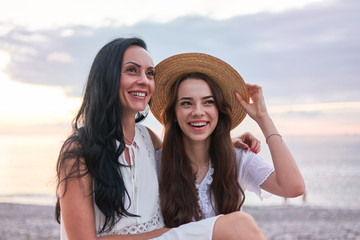 Portrait of happy attractive smiling hugging daughter with mother and having fun together in summertime at sunset by the sea