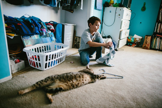 Boy in his bedroom with his cat putting away his laundry