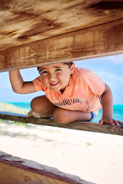 Little boy looking at the camera from under the table at a beach